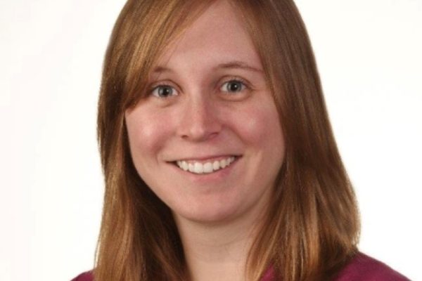 Sarah Timreck of IFES. She's a white woman with shoulder-length ginger hair and blue eyes. She's wearing a red blazer and smiles as she looks into the camera.